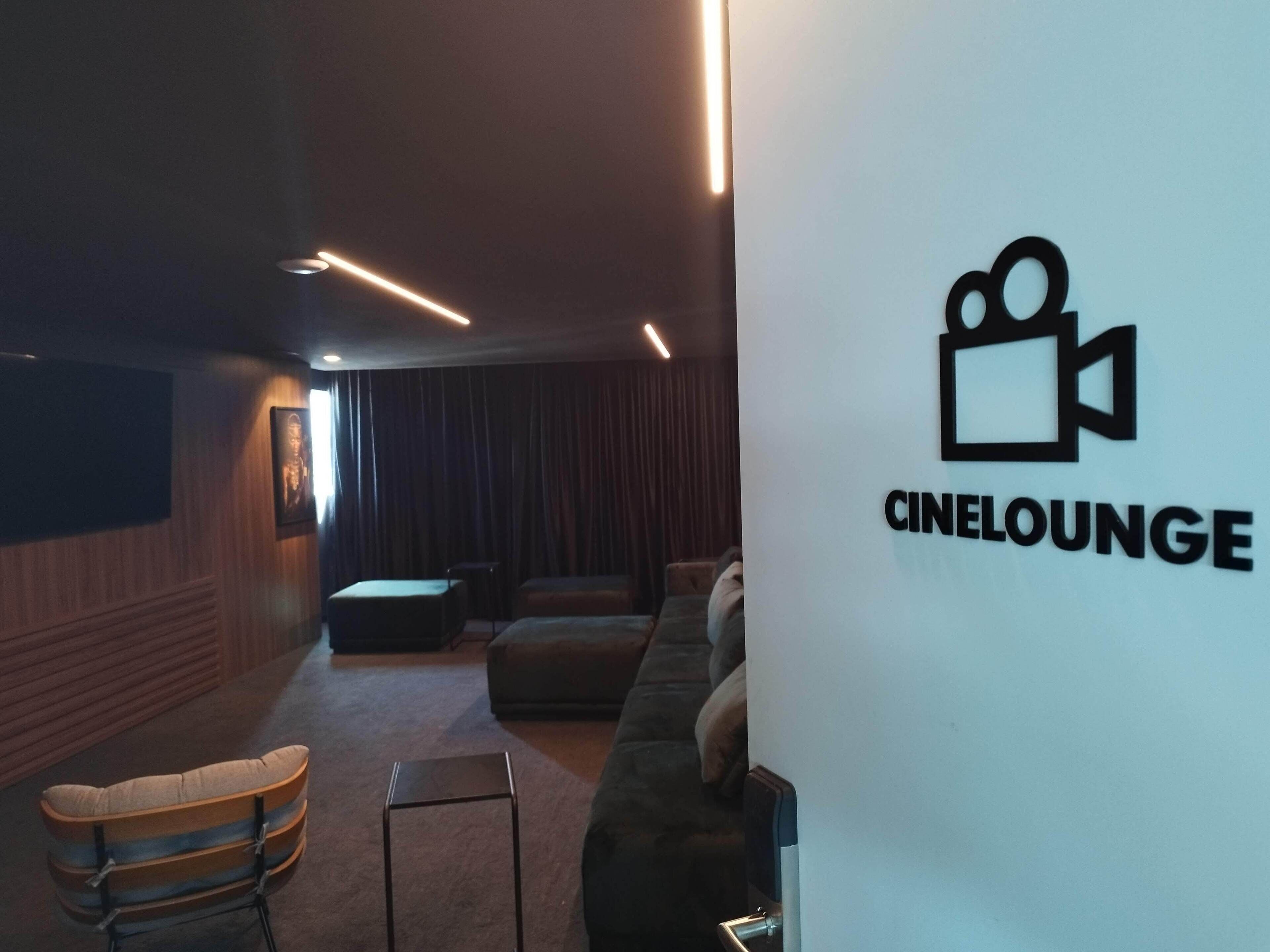 Un salon sur le thème du cinéma, avec le logo d’une caméra de cinéma fixé au mur, un canapé, une petite table et un banc rembourré.