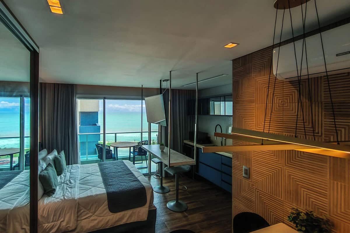 A modern hotel room with a large bed, a desk, and a view of the ocean.