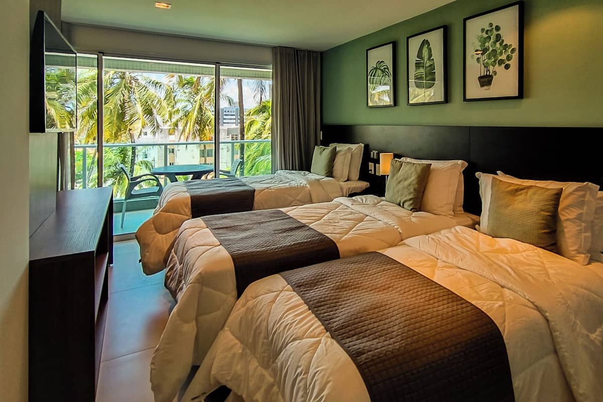 A hotel room with two beds, a desk, and a balcony with a view of palm trees.