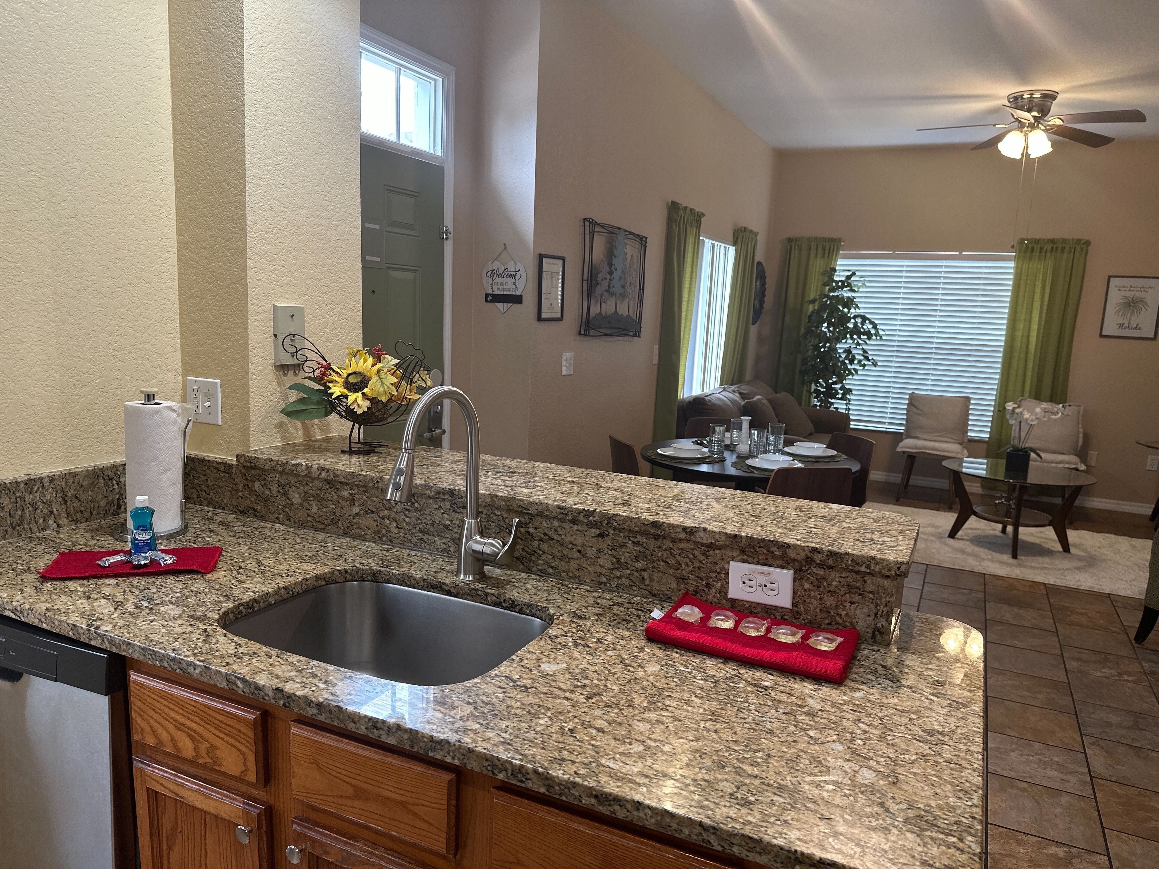 A kitchen with granite countertops, a stainless steel sink, wooden cabinets, and a dining area with a table set for four.