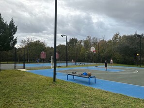 Una cancha de baloncesto exterior con superficie azul, un aro de baloncesto y una banca con una bolsa y zapatos.