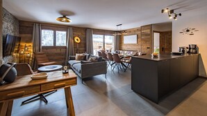 A modern kitchen with a central island, dining area with chairs, and a cozy seating area with a sofa and armchairs.