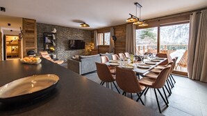 A modern dining area with a long table, cushioned chairs, and a stone accent wall.