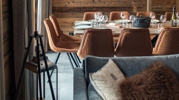 A dining area with a wooden wall, a large table set for four, and a floor lamp.