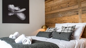 A neatly made bed with white linens, grey and black pillows, and a grey throw blanket. A black and white feather artwork is on the wall above the bed.