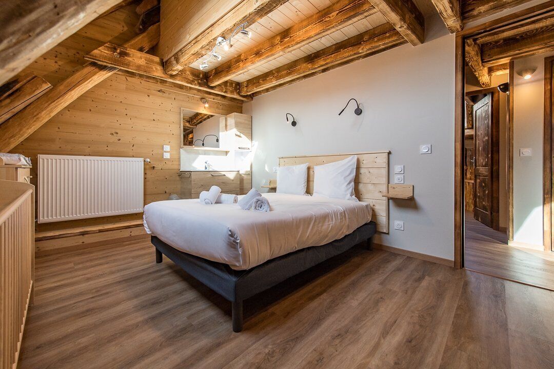 Un dormitorio con techo de madera, una cama con ropa blanca, un radiador y suelo de madera.