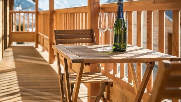 A wooden deck with a table and chairs, a bottle of wine, and two glasses.