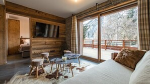 A cozy room with a large window, wooden walls, a sofa, a small table, and a TV mounted on the wall. - Top of the range flat with a large terrace in the heart of the village - sleeps 6 (ST SORLIN D ARVES)