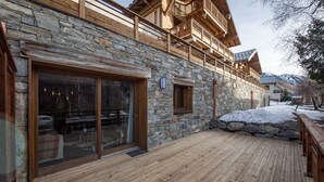 A wooden deck with stone walls, a large sliding glass door, and a stone staircase leading to a wooden balcony. - Top of the range flat with a large terrace in the heart of the village - sleeps 6 (ST SORLIN D ARVES)