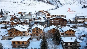Un pueblo cubierto de nieve con edificios de madera tradicionales, incluyendo un chalet destacado con balcón y un telesilla visible al fondo.
