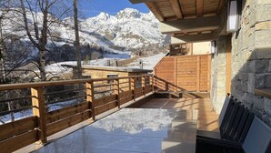Una terraza de madera con una mesa de vidrio, con vista a un paisaje montañoso nevado.