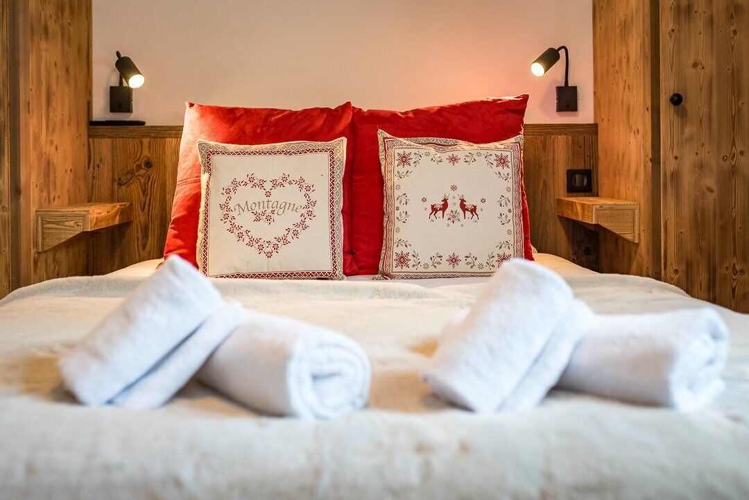 A neatly made bed with red and white pillows, two bedside lamps, and a wooden headboard.
