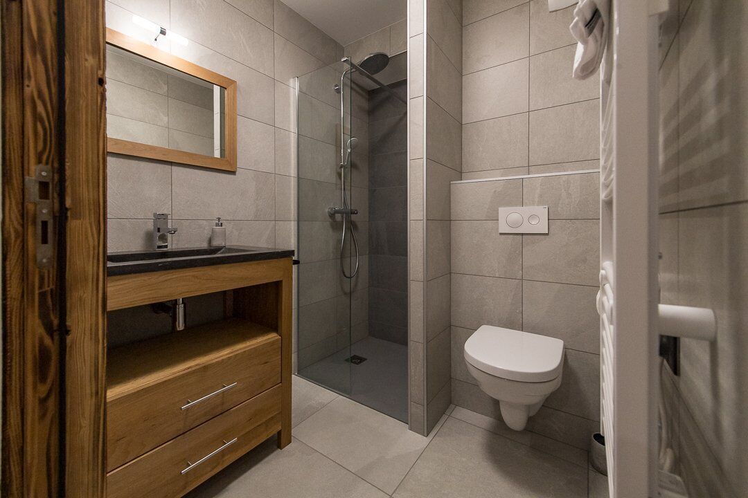 Un baño moderno con tocador de madera, ducha con cerramiento de vidrio y retrete blanco.