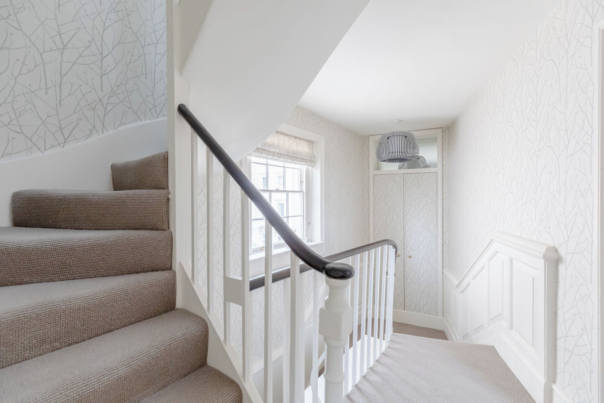 A staircase with a handrail, a window with a view, and a door with a patterned wallpaper.