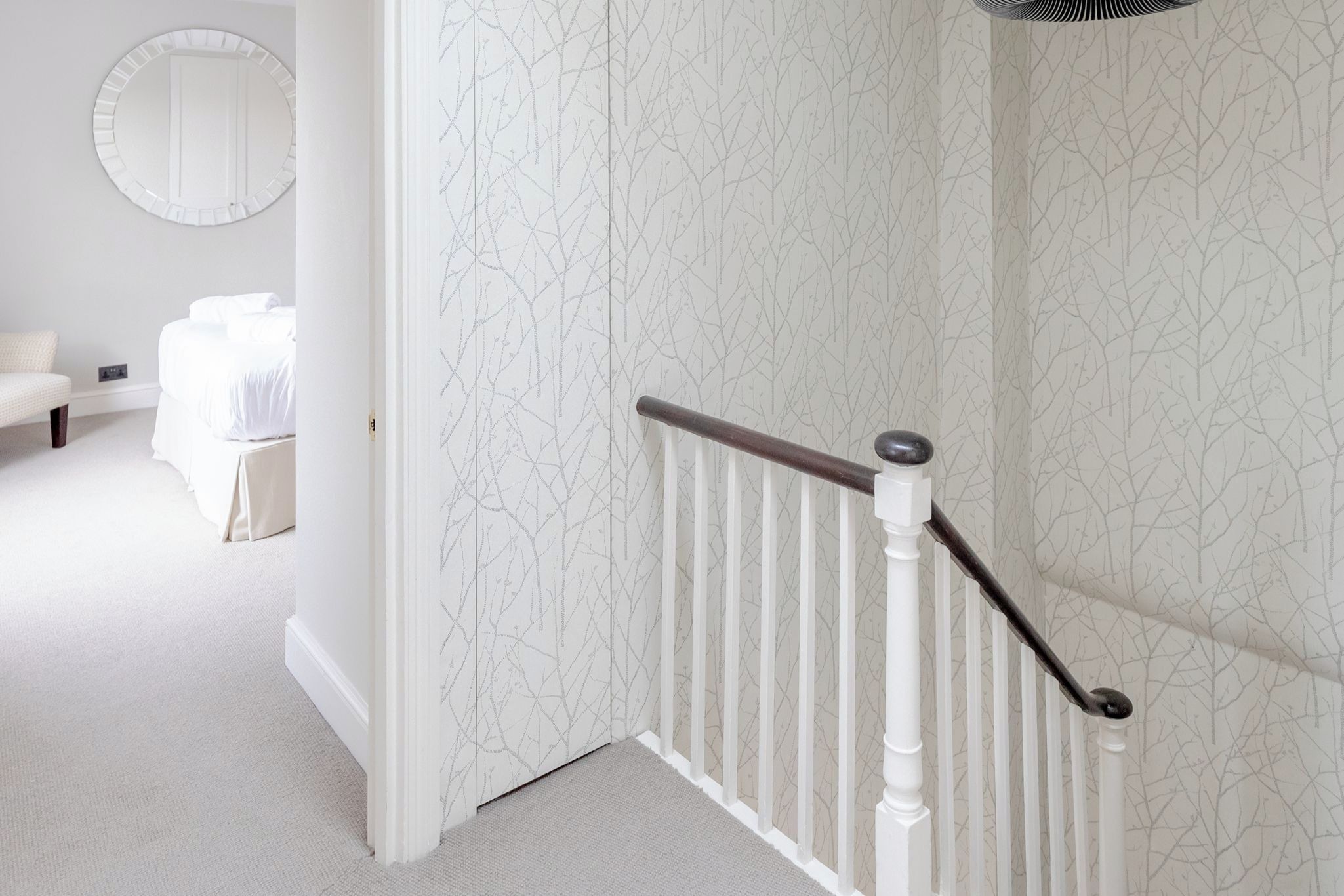 Eine Treppe mit weißen Geländern und einem dunklen Handlauf, die zu einem Raum mit einem Bett und einem runden Spiegel an der Wand führt.