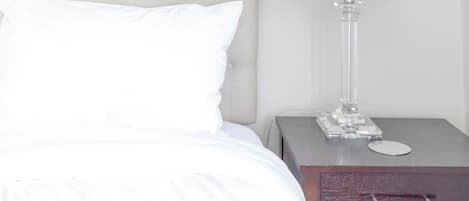 A bed with white bedding, a nightstand with a lamp, and a drawer.