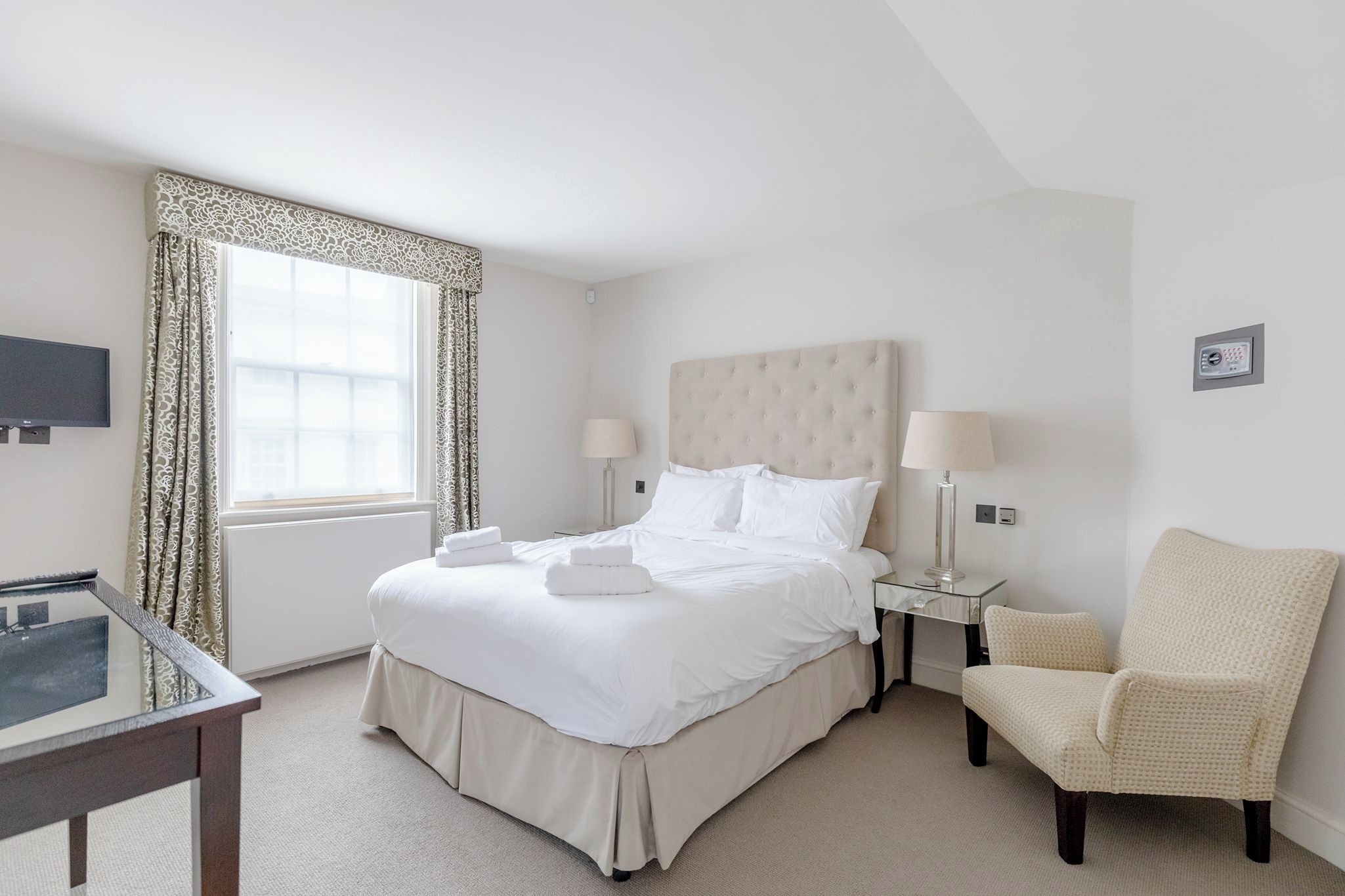 A hotel room with a bed, bedside lamps, a chair, a TV, and a window with curtains.