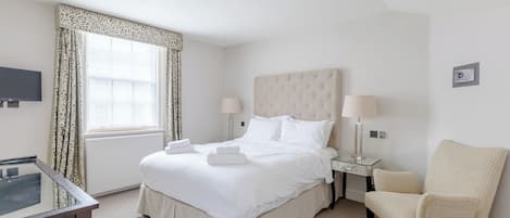 A hotel room with a bed, bedside lamps, a chair, a TV, and a window with curtains.