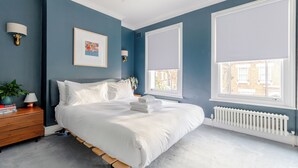 A bedroom with a bed, bedside tables, a radiator, and a window with blinds. - Beautifully Designed 2BD House - by Queen's Park! (London)
