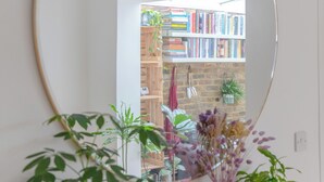 A room with a large mirror, a wooden table with potted plants, and a bookshelf filled with books. - Beautifully Designed 2BD House - by Queen's Park! (London)