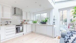 A modern kitchen with white cabinets, a built-in oven, and a large window. - Beautifully Designed 2BD House - by Queen's Park! (London)