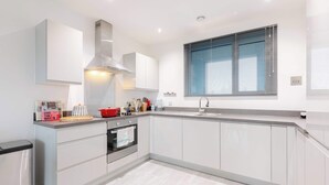A modern kitchen with white cabinetry, a stainless steel range hood, a built-in oven, and a window with blinds. - Bright 1 BDR Flat Balcony Heart of Brixton (Brixton)