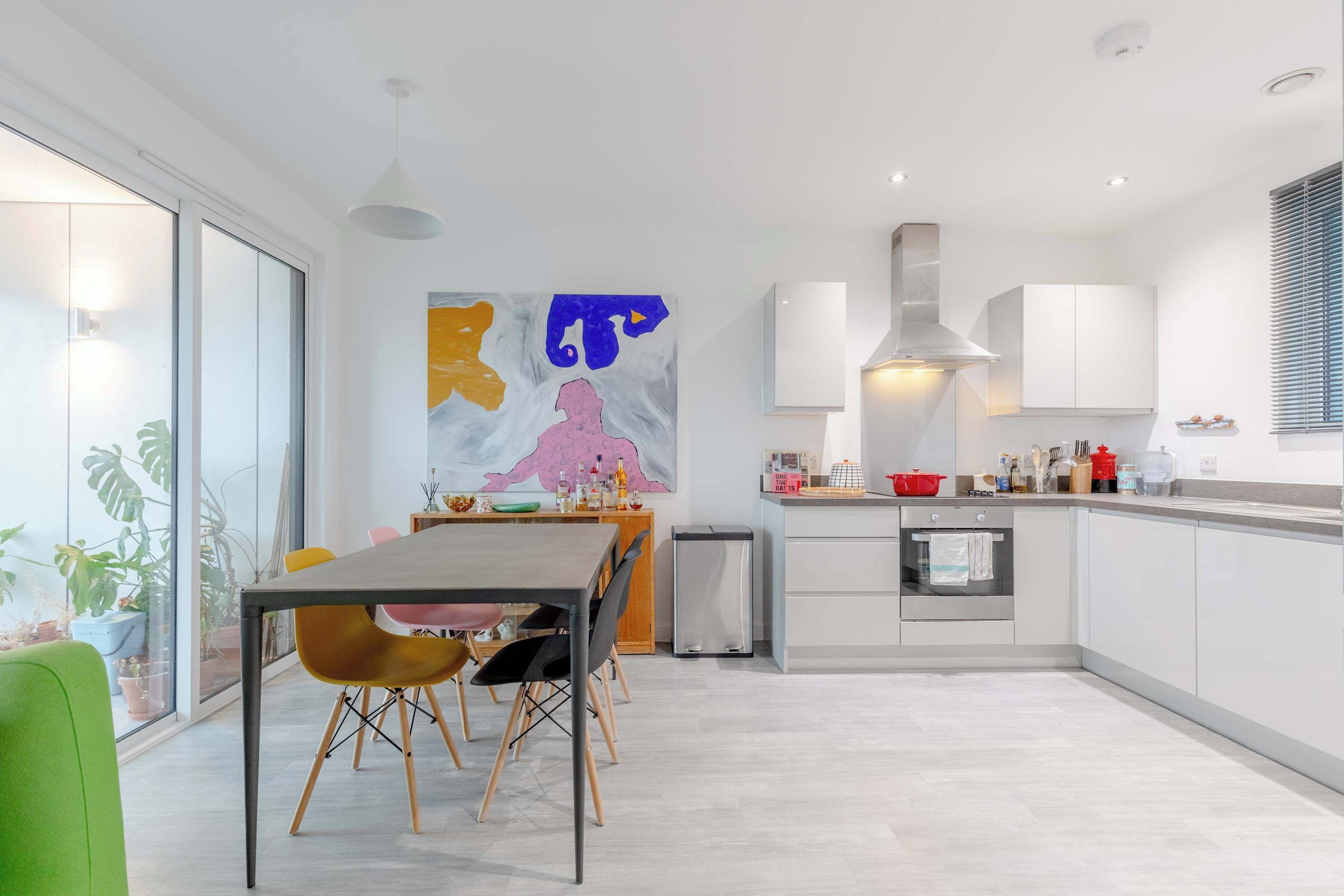 Una cocina moderna con armarios blancos, un comedor con mesa y sillas, y un cuadro abstracto grande en la pared.