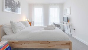 A modern bedroom with a wooden bed, white bedding, a desk with a computer, and a large abstract painting on the wall. - Bright 1 BDR Flat Balcony Heart of Brixton (Brixton)