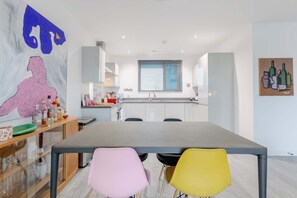 A modern kitchen with a dining area, featuring a large table, chairs, and a window with blinds. - Bright 1 BDR Flat Balcony Heart of Brixton (Brixton)