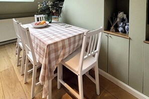 A dining area with a checkered tablecloth, white chairs, a bowl of fruit, and a vase with flowers. - Resplendent Riverside Residence | 3 Bed | Fulham (London)