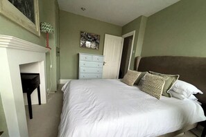 A bedroom with a bed, a dresser, a desk, and a fireplace. - Resplendent Riverside Residence | 3 Bed | Fulham (London)
