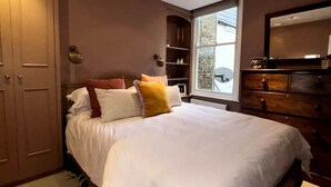 A bedroom with a large bed, wooden wardrobe, and a window with a view of the outside. - Resplendent Riverside Residence | 3 Bed | Fulham (London)