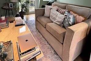 Een woonkamer met een beige bank, een salontafel, een laptop, boeken en decoratieve kussens.
