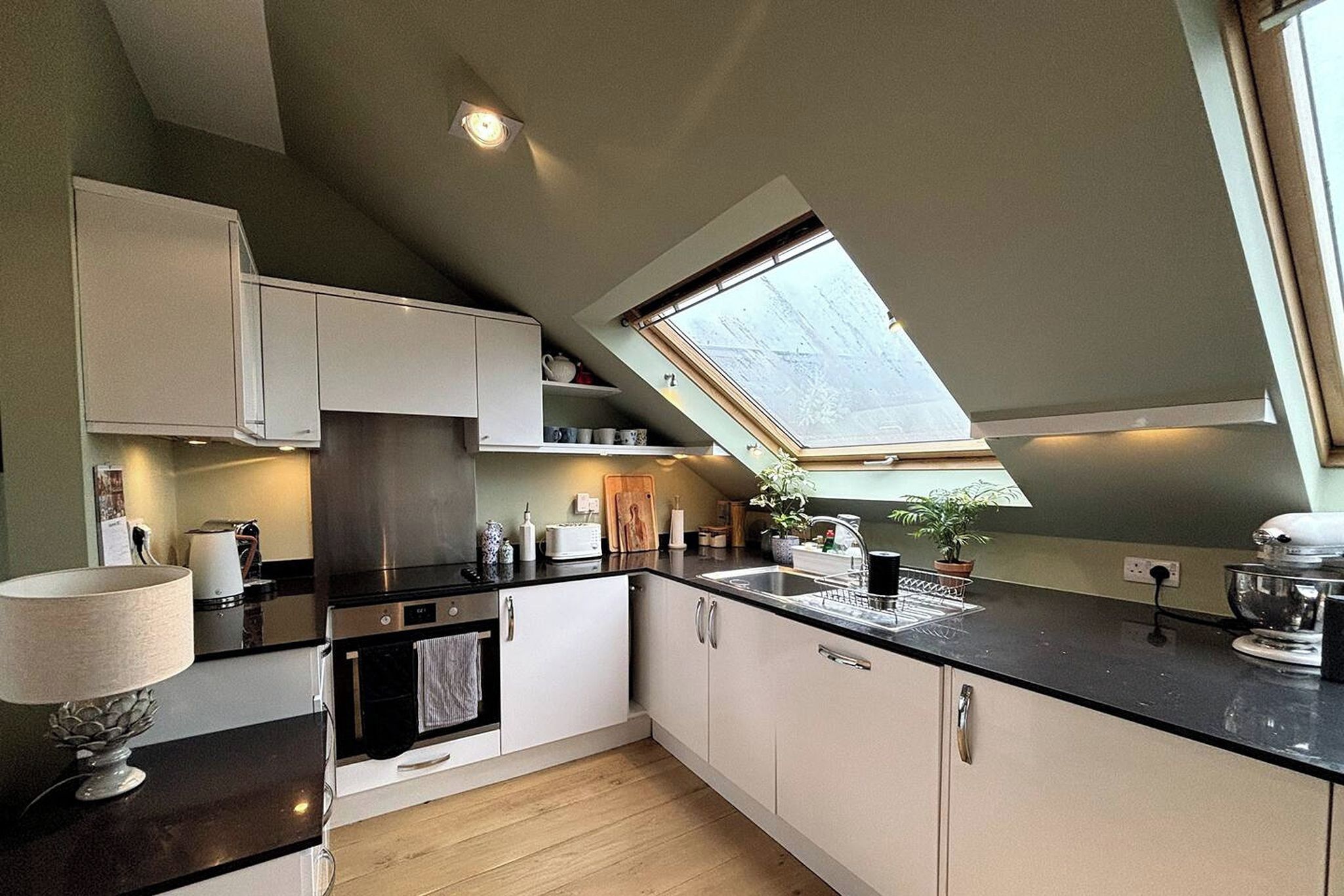 Une cuisine moderne dotée d’une verrière, d’appareils électroménagers intégrés et d’un plancher en bois.
