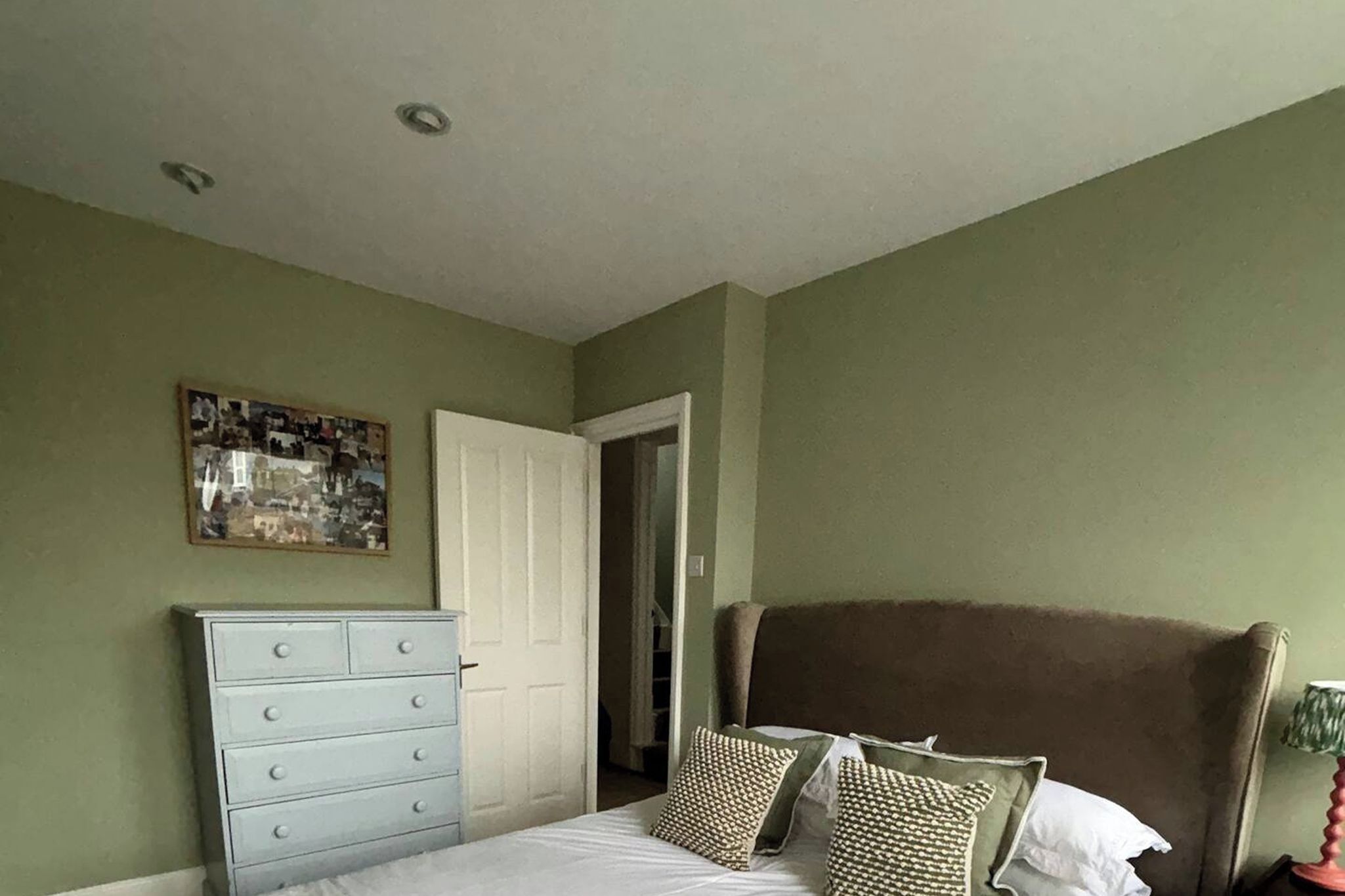 Ein Schlafzimmer mit Bett, Kommode und einer Tür zu einem anderen Raum.