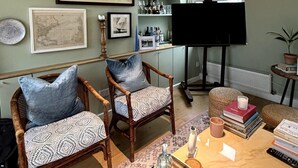 A living room with two wicker chairs, a coffee table, a bookshelf, and a piano. - Resplendent Riverside Residence | 3 Bed | Fulham (London)