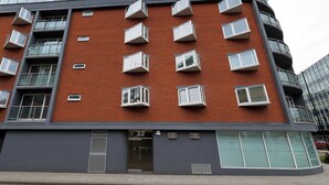 Um edifício de vários andares com fachada de tijolos vermelhos, várias varandas e entrada no nível da rua identificada com o número 32.
