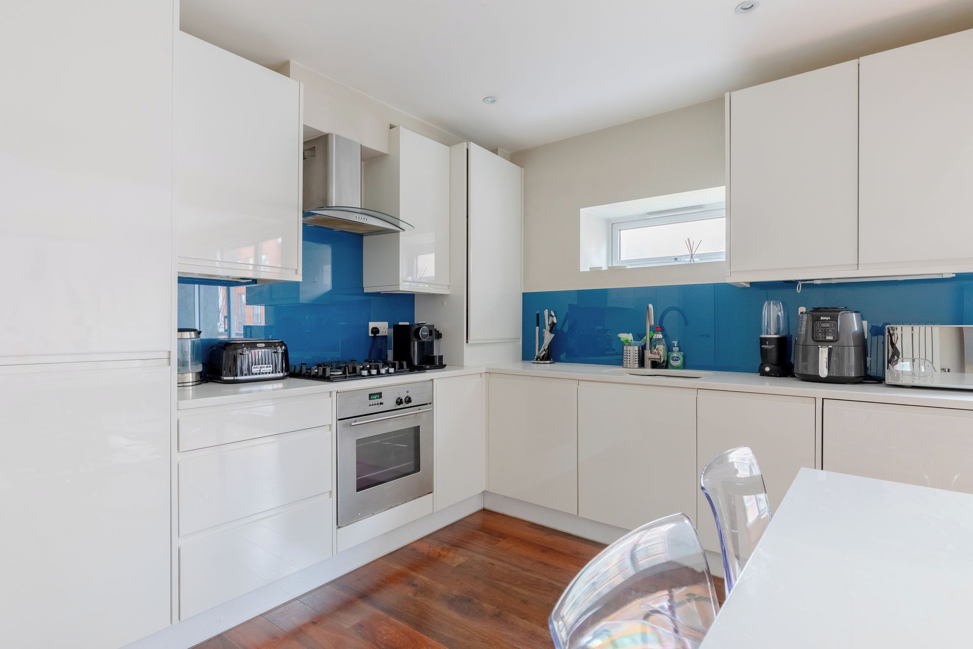 A modern kitchen with white cabinets, a blue backsplash, stainless steel appliances, and a window above the sink.