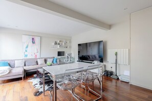 A modern living room with a glass dining table, a sofa, a flat-screen TV, and a radiator.