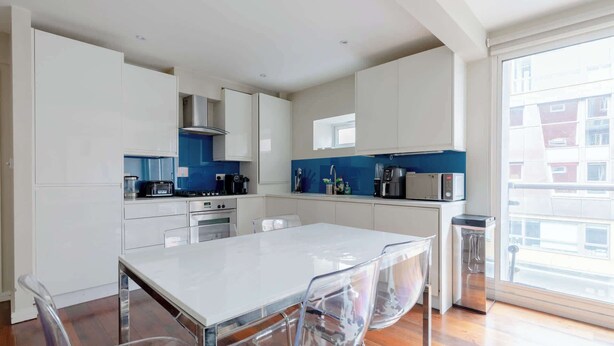 Uma cozinha moderna com armários brancos, uma ilha central com cadeiras e uma janela grande que oferece vista para o exterior.