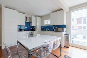 Une cuisine moderne avec des meubles blancs, un îlot central doté de chaises et une grande fenêtre offrant une vue sur l’extérieur.