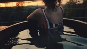 Uma pessoa sentada em uma piscina, com o pôr do sol ao fundo.