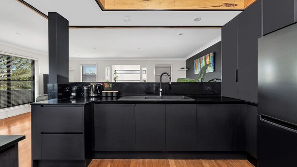 A modern kitchen with black cabinetry, a black countertop, and a wooden floor.
