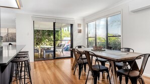 A modern dining area with a wooden table and chairs, a glass partition, and a view of an outdoor patio.