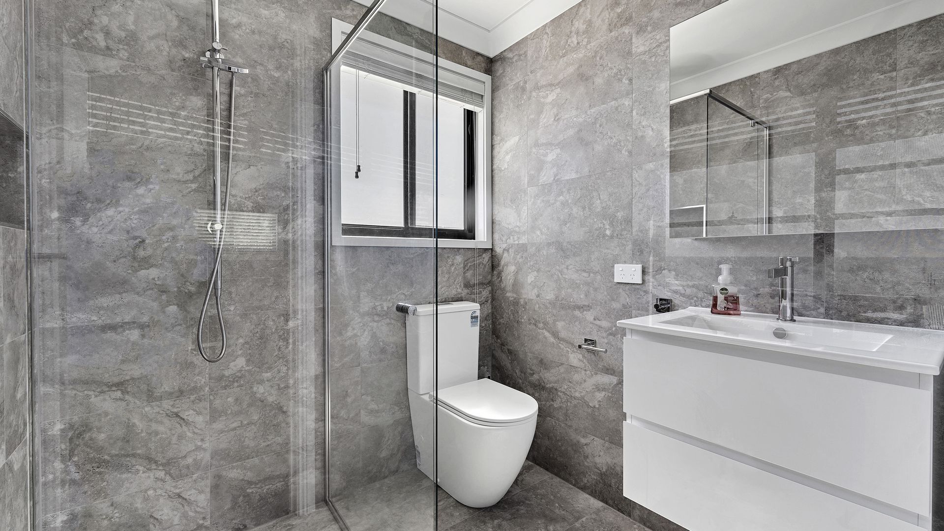 Un baño moderno con ducha de vidrio, inodoro blanco y tocador con espejo.