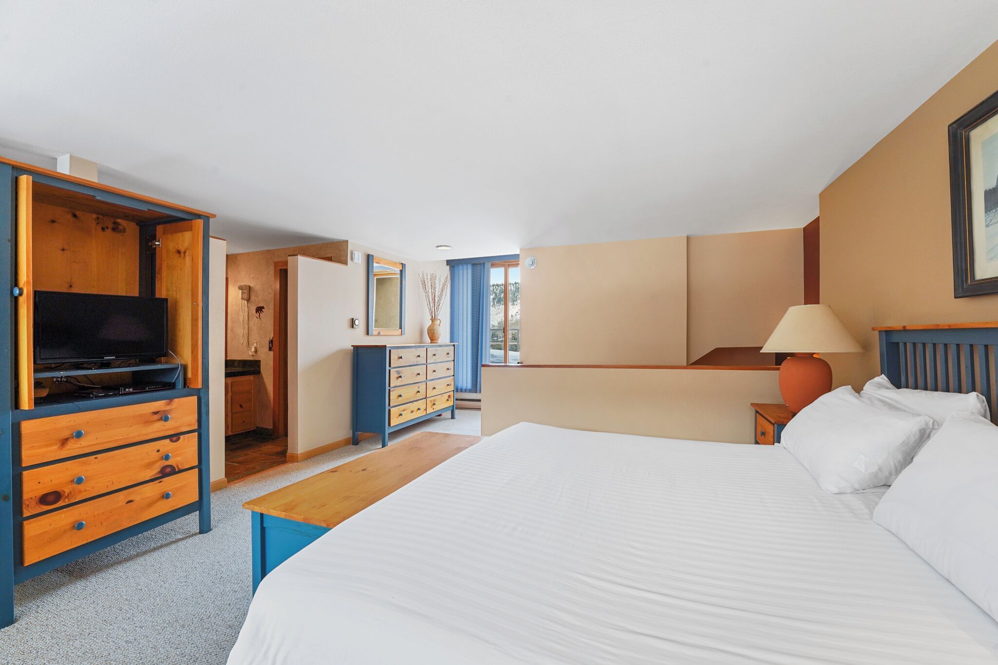 A hotel room with a bed, a TV, a dresser, and a desk.