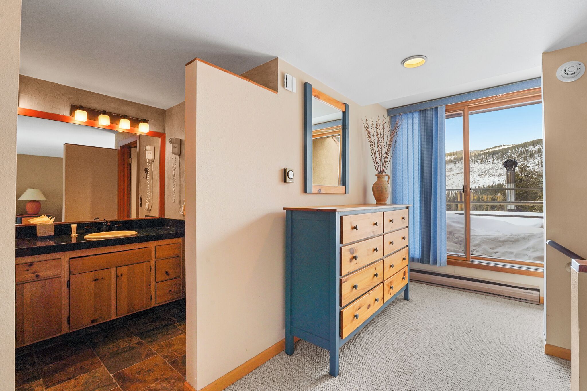 A bathroom with a wooden vanity, a mirror, and a window with a snowy view.