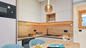 A modern kitchen with a microwave, sink, and wooden accents. There is a dining table with chairs, a vase of flowers, and a glass of wine. - Hedera Estate, Hedera A44 (Dubrovnik)