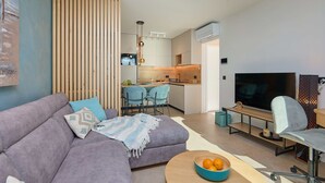 A modern living room with a sofa, a TV, and a dining area with chairs and a kitchen in the background. - Hedera Estate, Hedera A44 (Dubrovnik)
