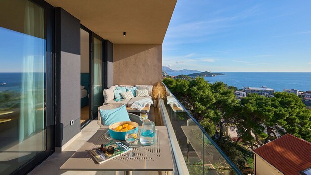A balcony with a table set for dining, a sofa, and a view of the sea and cityscape. - Hedera Estate, Hedera A44 (Dubrovnik)